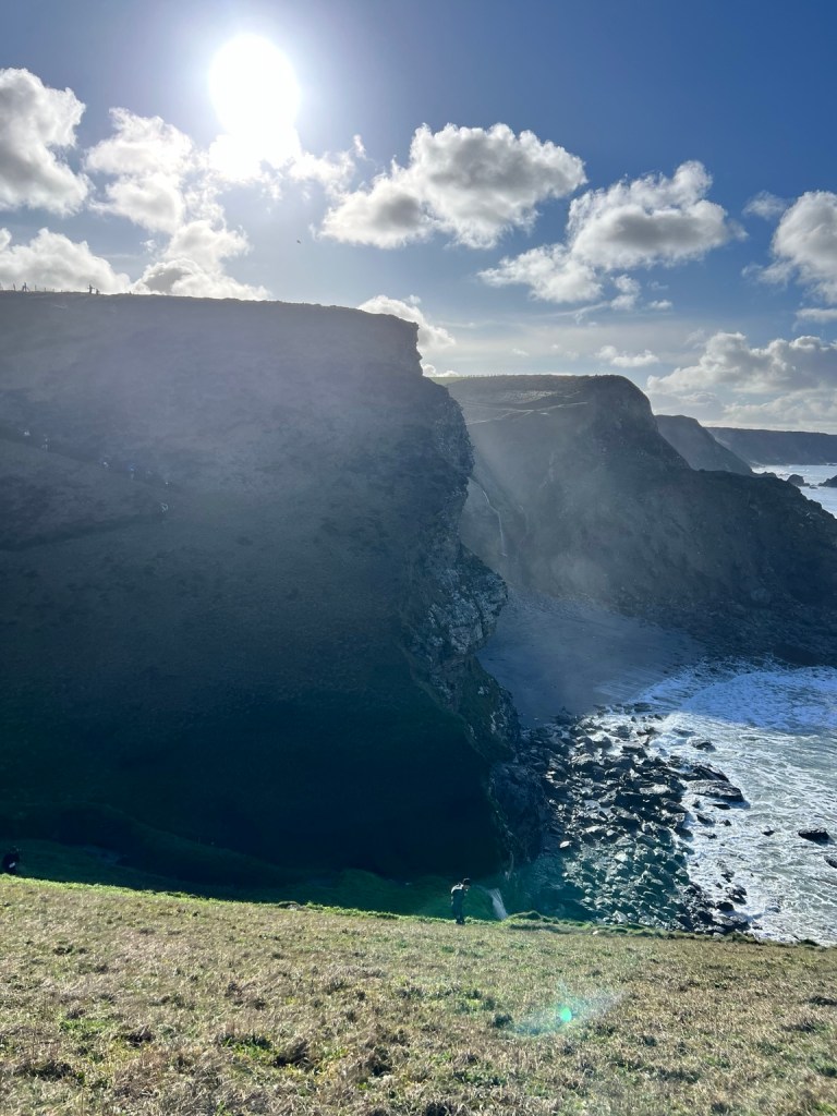 Sunlit coastal cliffs and sea beneath a blue sky.
