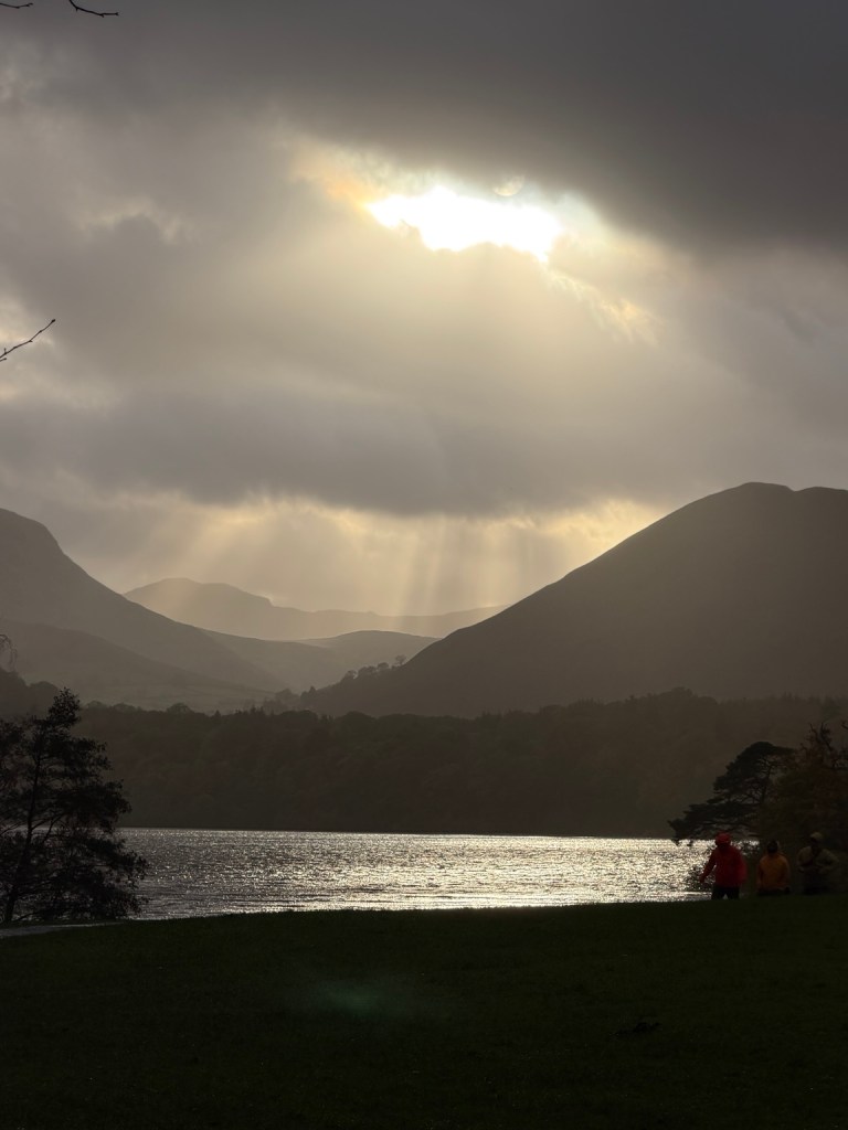 Sunlight breaking through storm clouds over a lake and fells in the Lake District